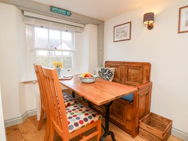 A dining area with a wooden table two chairs with polka dot cushions and a wooden bench under a window at Pepper's Cottage in Appledore