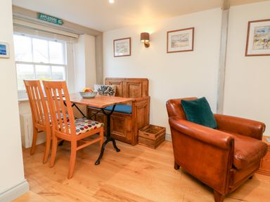 A corner dining area with wooden chairs and table beside a window and a leather armchair in a room at Pepper's Cottage in Appledore