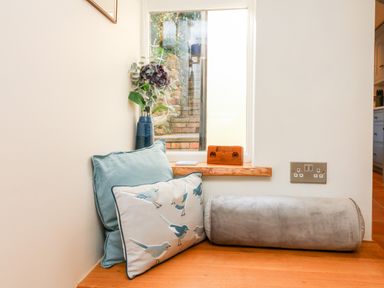 A small seating area with three cushions a vase with flowers on the windowsill and an electrical outlet on the wall at Pepper's Cottage in Appledore
