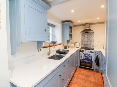 A kitchen with blue cabinets white countertops a stainless steel sink and stove with tiled backsplash at Peppers Cottage in Appledore