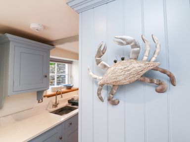 A kitchen with blue cabinets white countertop and a metal crab decoration on the wall at Peppers Cottage in Appledore