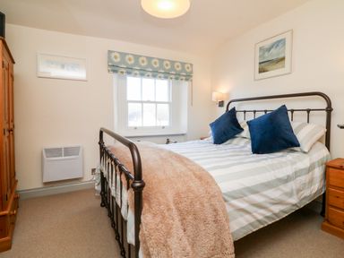 A bedroom with a metal bed frame two blue pillows a wooden wardrobe and window at Peppers Cottage in Appledore