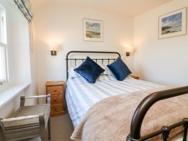 A bedroom with a double bed with striped bedding and blue pillows wooden bedside tables and framed pictures on the walls at Peppers Cottage in Appledore