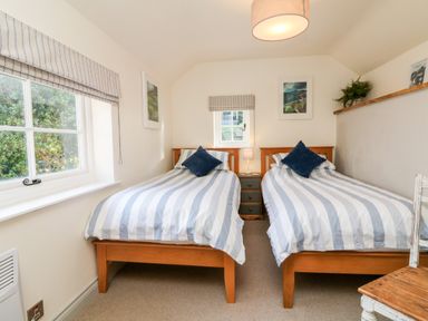 A bedroom with two single beds with striped bedding and blue pillows at Pepper's Cottage in Appledore