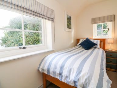 A bedroom with a single bed with striped bedding two windows and a bedside table with a lamp at Peppers Cottage in Appledore