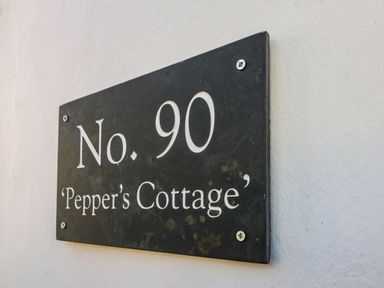 A black house number sign with white text No 90 Peppers Cottage on a white wall at Peppers Cottage in Appledore