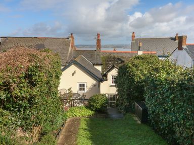 A garden with trimmed hedges and outdoor furniture behind houses at Peppers Cottage in Appledore