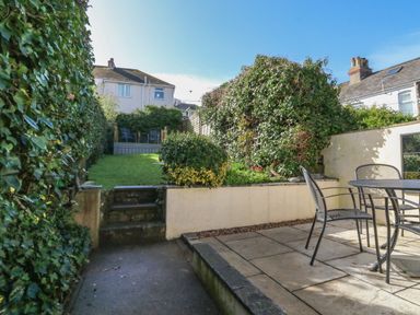 An outdoor patio area with a table and chairs next to a garden with steps and plants at Peppers Cottage in Appledore