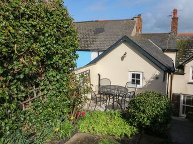 An outdoor patio with a round metal table and four chairs next to a cream-colored house with a small window at Peppers Cottage in Appledore