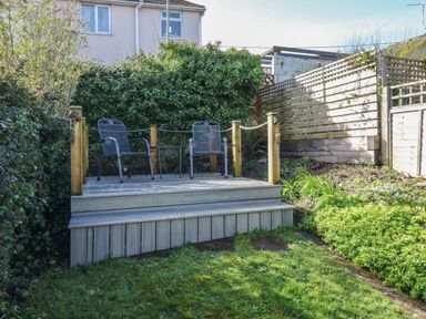 A small wooden deck with two metal chairs and a small table in a garden at Peppers Cottage in Appledore