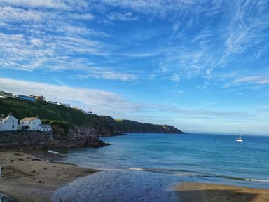 A coastal scene with a sandy beach houses on a hillside cliffs and a boat on the water at Mariners Rest in Gorran Haven