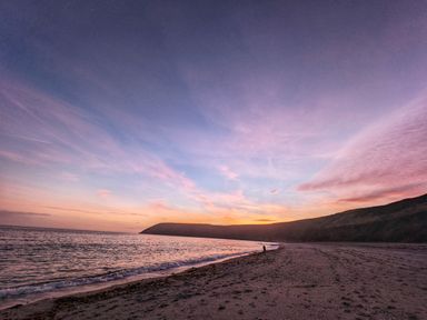 A beach with waves and a person walking near the shoreline at Mariners Rest in Gorran Haven