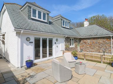 An outdoor patio area with two cushioned wicker chairs and a wicker table in front of a house at Mariners Rest in Gorran Haven