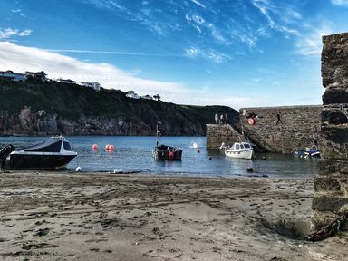 A small harbor with boats moored near a stone pier and cliffs in the background at Mariners Rest in Gorran Haven