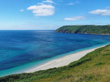 A coastline with a sandy beach and green cliffs beside a blue sea under a blue sky at Mariners Rest in Gorran Haven