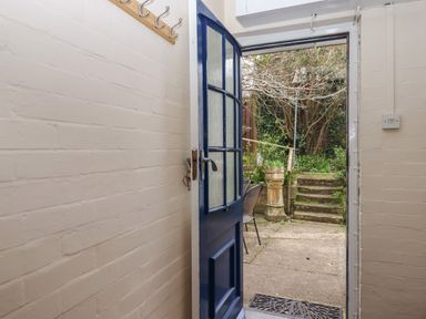 An open blue door leading from a small hallway with white brick walls to an outdoor area with stone steps and garden vegetation at Greenhedges in Budleigh Salterton