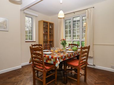 A dining room with six wooden chairs around a table covered with a colorful checkered tablecloth at Greenhedges in Budleigh Salterton
