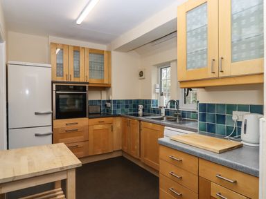 A kitchen with wooden cabinets blue tiled backsplash a refrigerator oven sink and small wooden table at Greenhedges in Budleigh Salterton