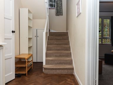 A hallway with carpeted stairs wooden parquet floor a wooden bench and white shelves at Greenhedges in Budleigh Salterton