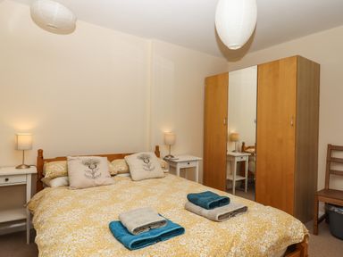 A bedroom with a double bed with yellow floral bedding two bedside tables with lamps a wooden wardrobe with mirrored door and a wooden chair at Greenhedges in Budleigh Salterton