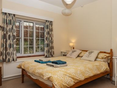 A bedroom with a wooden bed with yellow floral bedding and folded towels on top at Greenhedges Budleigh Salterton