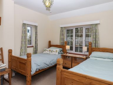 A bedroom with two wooden single beds a wooden chair and bedside table with lamps at Greenhedges Budleigh Salterton