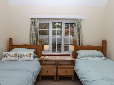 A bedroom with two single wooden beds a wooden nightstand with two lamps and a window with patterned curtains at Greenhedges in Budleigh Salterton