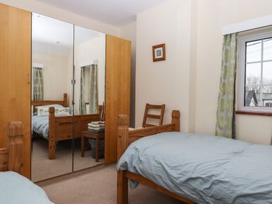 A bedroom with two single wooden beds a mirrored wardrobe a chair a window with patterned curtains and a small framed picture on the wall at Greenhedges in Budleigh Salterton