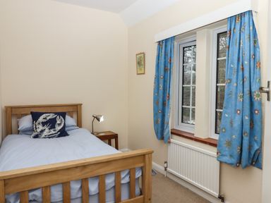 A bedroom with a wooden bed a bedside table with a lamp blue curtains and a window at Greenhedges in Budleigh Salterton