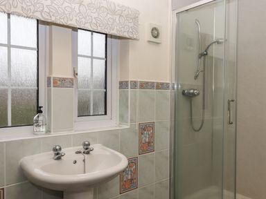 A bathroom with a sink faucet soap dispenser window and a shower cubicle with glass door at Greenhedges Budleigh Salterton