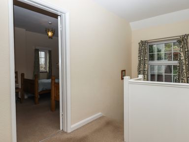 A stair landing with beige carpet and white railing leading to a bedroom with wooden bed and window with curtains at Greenhedges in Budleigh Salterton