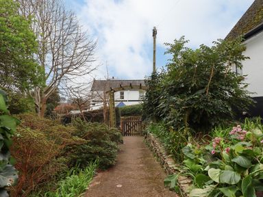 A garden path with plants on both sides leading to a wooden gate and a trellis at Greenhedges in Budleigh Salterton
