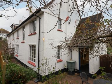 Exterior of a white building with red window sills and a black rain gutter with garden and patio furniture at Greenhedges Budleigh Salterton