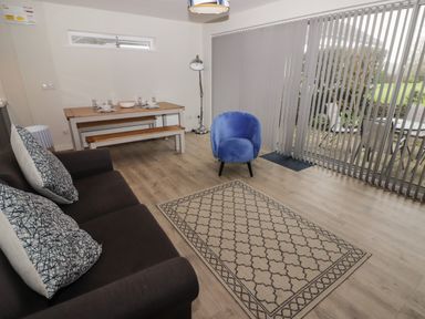 A living room with a brown sofa and cushions a blue armchair a wooden dining table with benches and a floor lamp at 16 Coedrath Park in Saundersfoot