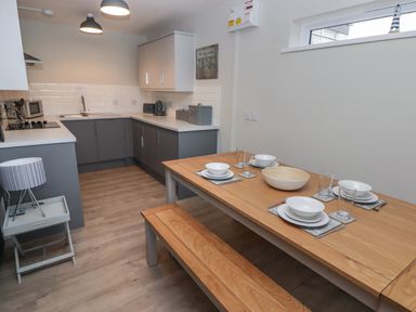 A kitchen with grey cabinets and a wooden dining table set with plates bowls and glasses at 16 Coedrath Park in Saundersfoot
