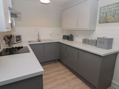 A kitchen with grey lower cabinets white upper cabinets a sink toaster kettle microwave and canisters at 16 Coedrath Park Saundersfoot