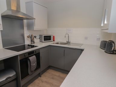 A kitchen with gray cabinets white countertops a stove microwave sink toaster and kettle at 16 Coedrath Park Saundersfoot