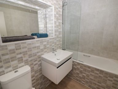 A bathroom with a toilet sink bathtub mirror and folded towels at 16 Coedrath Park in Saundersfoot