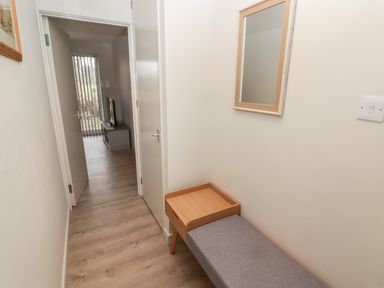 A hallway with a bench and a mirror on the wall showing an open door leading to a room with a TV and sliding glass door at 16 Coedrath Park in Saundersfoot