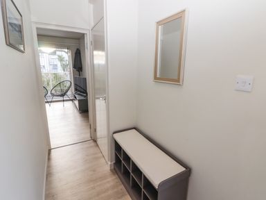 A narrow hallway with a cushioned shoe storage bench and a wall mirror leading to a living area with chairs and a TV at 36 Coedrath Park in Saundersfoot