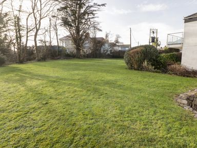 A grassy garden with bushes trees and houses in the background at 36 Coedrath Park in Saundersfoot