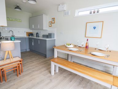 A kitchen with gray cabinets a wooden dining table set with plates glasses and wine at 36 Coedrath Park in Saundersfoot