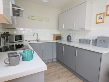 A kitchen with grey cabinets white countertops a microwave sink toaster kettle and labeled storage containers at 36 Coedrath Park Saundersfoot