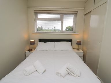 A bedroom with a bed with white sheets and towels on top two bedside tables with lamps under a window with blinds at 36 Coedrath Park in Saundersfoot