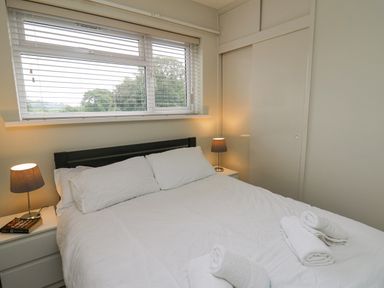A bedroom with a bed covered in white linens and rolled towels a window with blinds and two bedside tables with lamps 36 Coedrath Park Saundersfoot