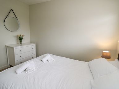 A bedroom with a bed and rolled towels a chest of drawers with a vase of flowers and a round wall mirror at 36 Coedrath Park Saundersfoot