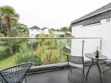 A balcony with a small round table and two chairs overlooking a garden with trees and shrubs at 36 Coedrath Park Saundersfoot
