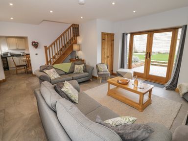 A living room with grey sofas a wooden coffee table and wooden doors leading outside at The Stables in Droitwich Spa