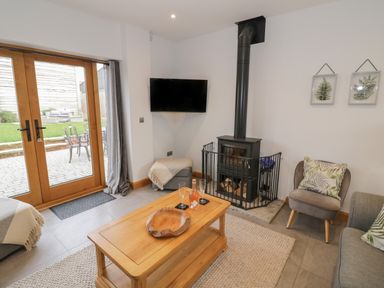 A living room with a wooden coffee table a wood-burning stove a wall-mounted TV and sliding glass doors at The Stables in Droitwich Spa