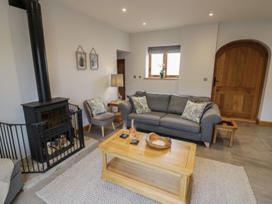 A living room with a gray sofa a wood burning stove and a wooden coffee table at The Stables in Droitwich Spa